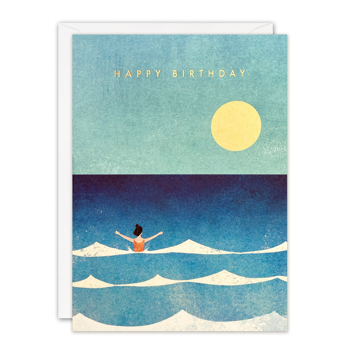 Birthday card of a woman swimming joyfully in white-crested waves under a large yellow sun, gold foil text