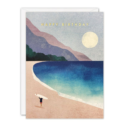 Birthday card of a surfer carrying a board across a pink beach towards a blue bay under a pale moon, gold foil