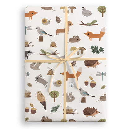 White wrapping paper with foxes, hedgehogs, rabbits, owls, birds, acorns and toadstools, tied with a peach ribbon