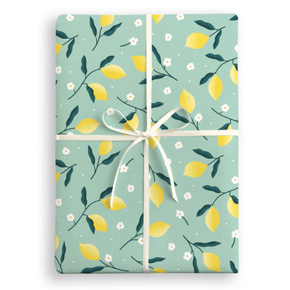 Sage green wrapping paper with yellow lemons, dark leaves and white blossom, tied with a cream ribbon
